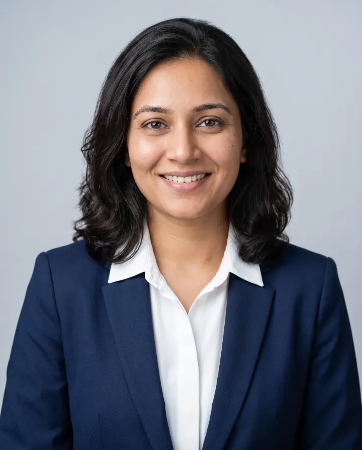 AI professional headshot of the same woman in a navy suit and white shirt on a light grey studio background